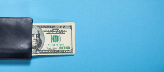 Black wallet with a dollar banknotes on the blue background.