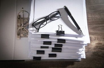 Stack of documents, eyeglasses and pen on table in office.
