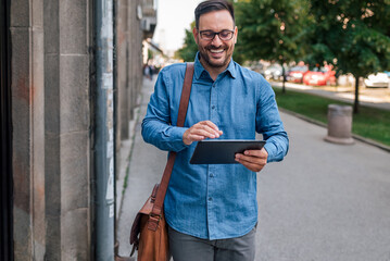 Male executive commuter is looking at hand held digital tablet screen while walking on sidewalk. © Moon Safari