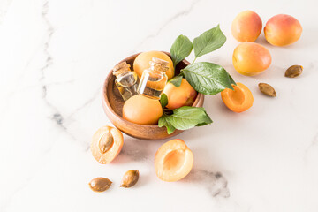 two glass bottles with cork lid with apricot oil and ripe apricots in a wooden bowl on a marble background. rejuvenation. skin care.