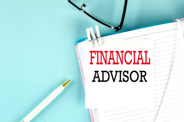 FINANCIAL text on a sticky on notebook with pen and glasses , blue background
