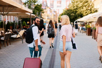 Happy young tourist couple walking through european city with suitcase