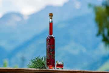 a glass and bottle fresh liquor from the swiss stone pine at a sunny july day with the mountains in the background