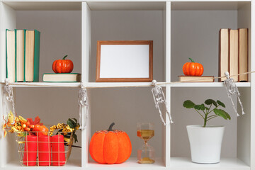 Halloween home interior decor. White shelves, photo frames, books, plant pots, pumpkins.