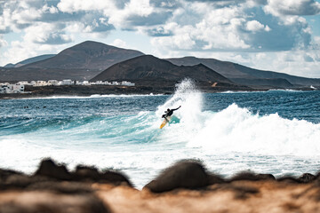 Côte rocheuse sauvage du spot de surf La Santa Lanzarote, îles Canaries, Espagne. Surfeur chevauchant une grosse vague dans la baie rocheuse, montagne volcanique en arrière-plan.