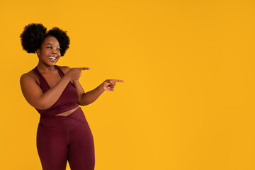 Happy smiling woman pointing at copy space on yellow studio background. Young sporty girl showing something on empty space.