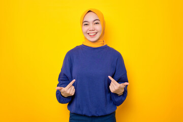 Cheerful young Asian Muslim woman dressed in casual sweater pointing at herself with proud isolated...