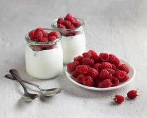 yogurt with raspberry and plate of raspberries and two spoons on the white table