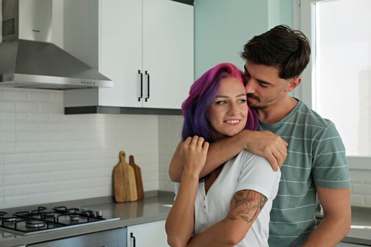Young woman with colorful hair and her husband in the open plan kitchen of their new home. Hipster couple having fun at the dining room. Copy space, interior background.