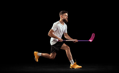 Studio shot of young man wearing sports uniform and sneakers playing floorball isolated on dark background. Sport, action and motion, movement, competition