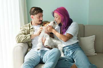 Happy hipster couple with their rough coated dog. Young woman with colorful pink purple hair and her bearded boyfriend playing with wire haired jack russell terrier. Close up, copy space, background.