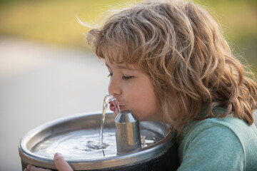Child drinking water from outdoor water fountain outdoor.