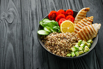 quinoa salad with grilled chicken and vegetables on a black wooden rustic background