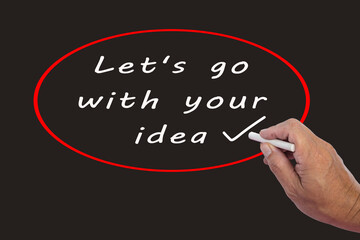 Male hand writes in white chalk pencil the word LETS GO WITH YOUR IDEA.