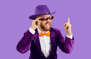 Overjoyed man entertainer in suit and hat isolated on purple studio background point up at sale...