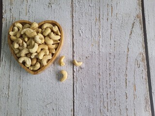 Cashew nuts in heart shaped bowl on wooden table, top view. Space for text