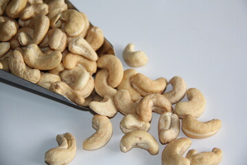 Cashew nuts in a stainless steel measuring spoon on a white background, top view. Space for text.