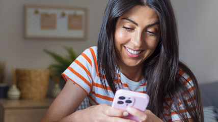 Beautiful  young smiling woman sitting at home and  using mobile phone