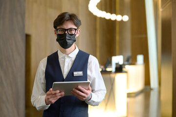 Young owner or receptionist of luxurious hotel with digital tablet looking at camera while standing...