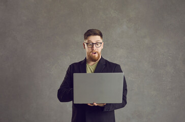 Studio portrait of shocked bearded business man holding laptop looking at screen and expressing surprise. Adult excited guy freelancer entrepreneur surprised about internet news, social media discount