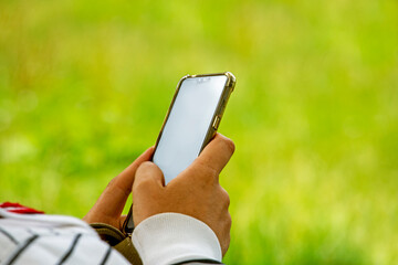 man hold in his hands a white smartphone lying on the grass at a picnic. Use Smartphone template for advertising.