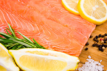 Salmon fillet with lemon and rosemary on a wooden board.