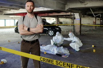 Young serious policeman standing in crime scene area against two criminological experts looking for...