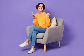 Fototapeta na wymiar Portrait of beautiful trendy cheerful girl sitting using gadget showing copy space idea isolated over violet lilac color background