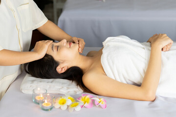 Obraz na płótnie Canvas Asian woman lying in bed doing spa with smiling, happy, relaxing face in candlelight. warm atmosphere She was massaged by the spa staff on her face and shoulders making her feel very comfortable.