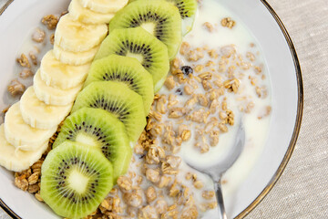 Breakfast with yogurt, kiwi and banana. Plate with granola and fresh fruit. healthy eating style.
View from above