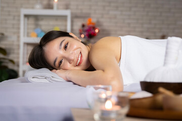 Obraz na płótnie Canvas Asian woman lying in bed doing spa with smiling, happy, relaxing face in candlelight. warm atmosphere with her facing the camera