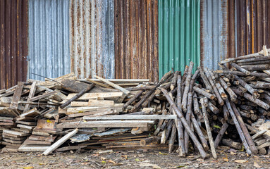 Low view, piles of logs of different sizes are piled on the ground near old galvanized walls.