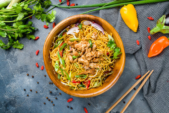 chicken wok noodles with vegetables on wooden bowl, egg noodles top view