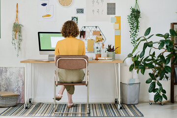 Back view of young businesswoman or freelancer working in front of computer monitor while sitting...