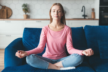Woman sitting on couch in lotus pose, doing meditation