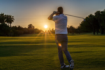 Good strike, professional golfer looking trajectory of the ball, golfer hitting golf ball standing on course at sunny evening