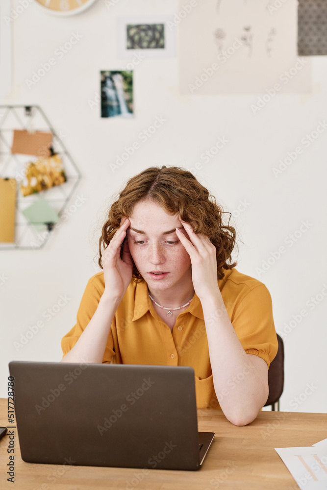 Poster young businesswoman expressing misunderstanding or tiredness while sitting by desk in front of lapto