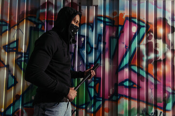 Side view of african american vandal holding baseball bat near graffiti on wall on street