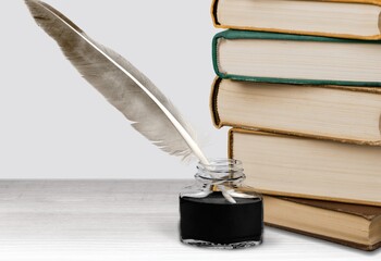 Feather quill pen with a vintage ink well and a stack of old books, the concept of writing