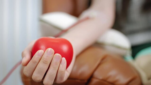 Close up of young woman donating blood and holding red ball in hand

