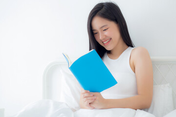 Young asian woman reading a book with relax and cozy on the bed in the bedroom at home, female leisure reading novel while resting with emotional positive, one person, lifestyles concept.