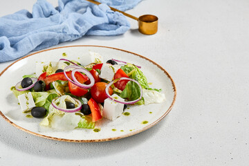 Classic greek salad with pesto sauce on ceramic plate. Vegetable salad with tomatoes, cucumber, paprika, onion and olives. Traditional grecian food. Greek salad on concrete background.