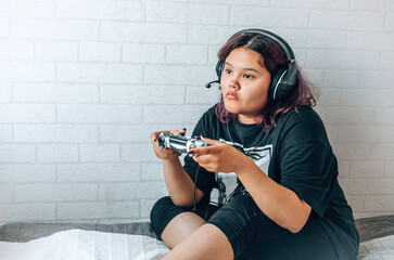 Asian girl with purple hair, generation Z, sitting on the bed, holding a joystick, playing a...