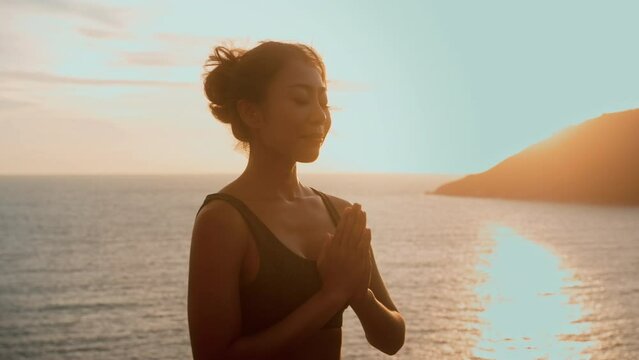 Young asian woman in sportswear doing yoga on the rock at seaside during Sunset, health and meditation concept.