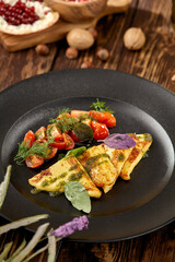 Grilled halloumi cheese with pesto sauce and tomatoes on black plate. Appetizer from fried cheese in greek style on wooden background. Hot appetizer of halloumi cheese in rustic style.