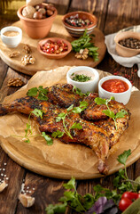 Traditional georgian dish - chicken tabaka on wooden background in rustic style. Roasted whole chicken in georgian style on wooden table. Chicken tabaka with sauces in rustic style.
