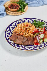 Traditional uzbek food - plov with beef. Eastern cuisine - pilaf with rice, meat and spices. Plov with beef on traditional uzbek plate. Composition of oriental ceramic plate with pilaf.