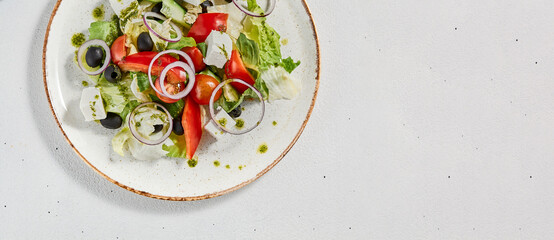Classic greek salad with pesto sauce on ceramic plate. Vegetable salad with tomatoes, cucumber, paprika, onion and olives. Traditional grecian food. Greek salad on concrete background.