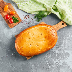 Classic pie with cabbage and eggs on wooden board. Composition with cabbage pie on concrete background with textile and spices. Homemade pie with cabbage in rustic style on gray table.