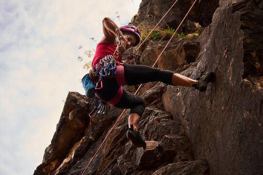 Senior Woman Climbing On Rocky Cliff Against Sky